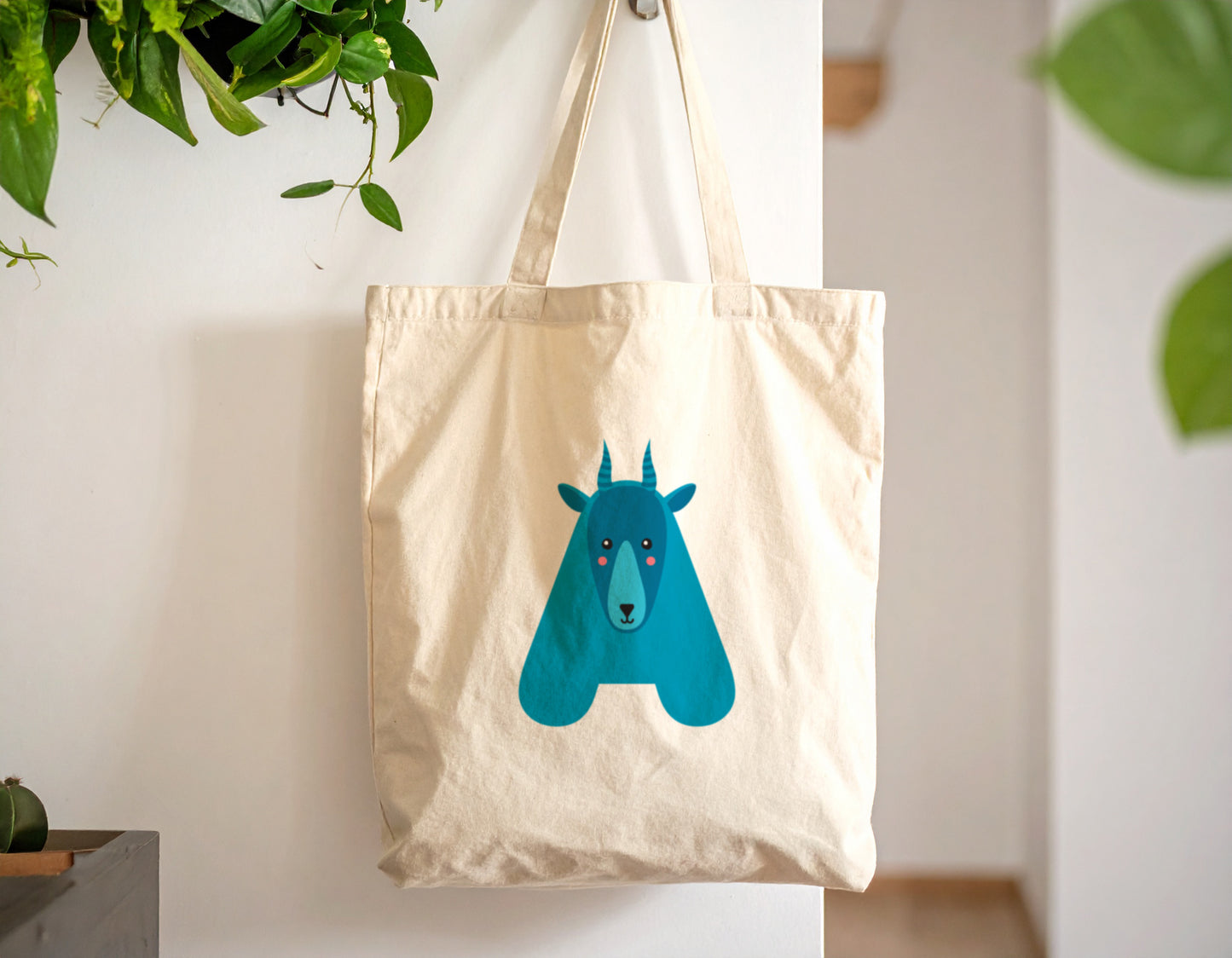 An oyster tote bag with the letter “A” in the shape of an antelope illustration, hanging against a white wall.