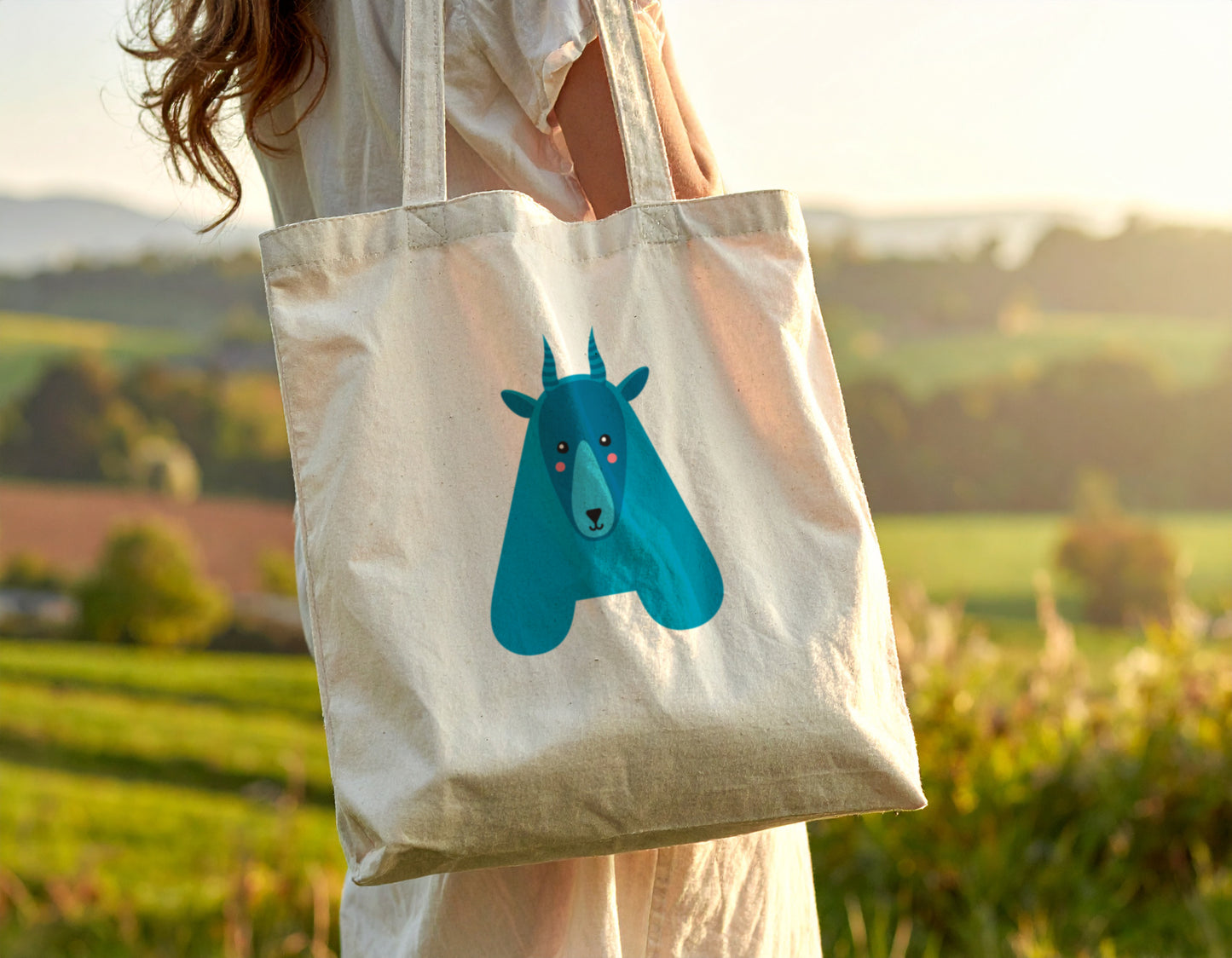A woman carrying a tote bag with the letter “A” in the shape of an antelope illustration, standing on a blurry autumn background.