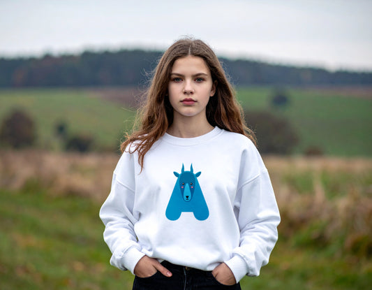 A teenage girl wearing a white crewneck sweatshirt with the letter A in the shape of an antelope illustration, standing, blurry outdoor setting.