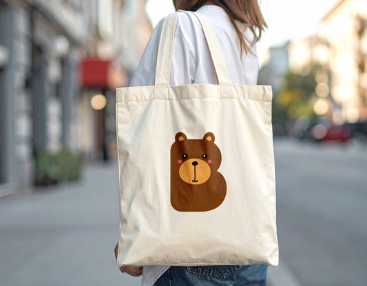 A woman carrying a tote bag with the letter B in the shape of a bear illustration, standing, blurry street background.