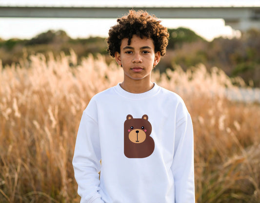 A teenage boy wearing a white crewneck sweatshirt with the letter B in the shape of a bear illustration, standing, blurry wheat field.