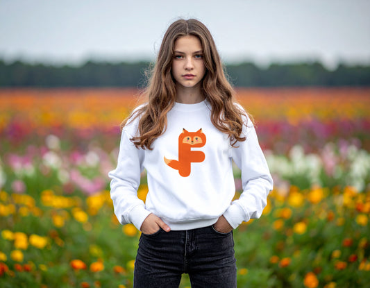A teenage girl wearing a white crewneck sweatshirt with the letter F in the shape of a fox illustration, standing  in a field of flowers.