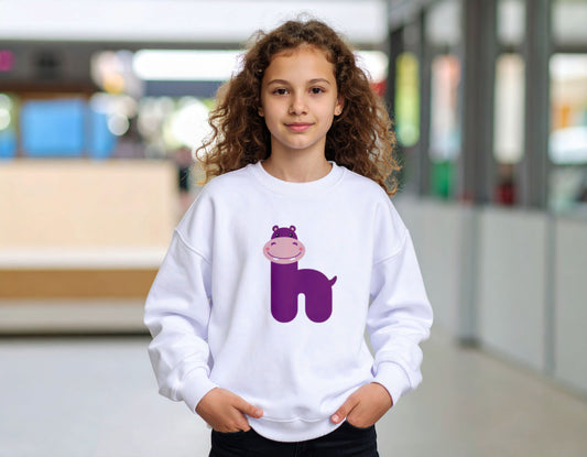A teenage girl wearing a white crewneck sweatshirt with the letter H in the shape of a hippo illustration, standing in a blurry school corridor.