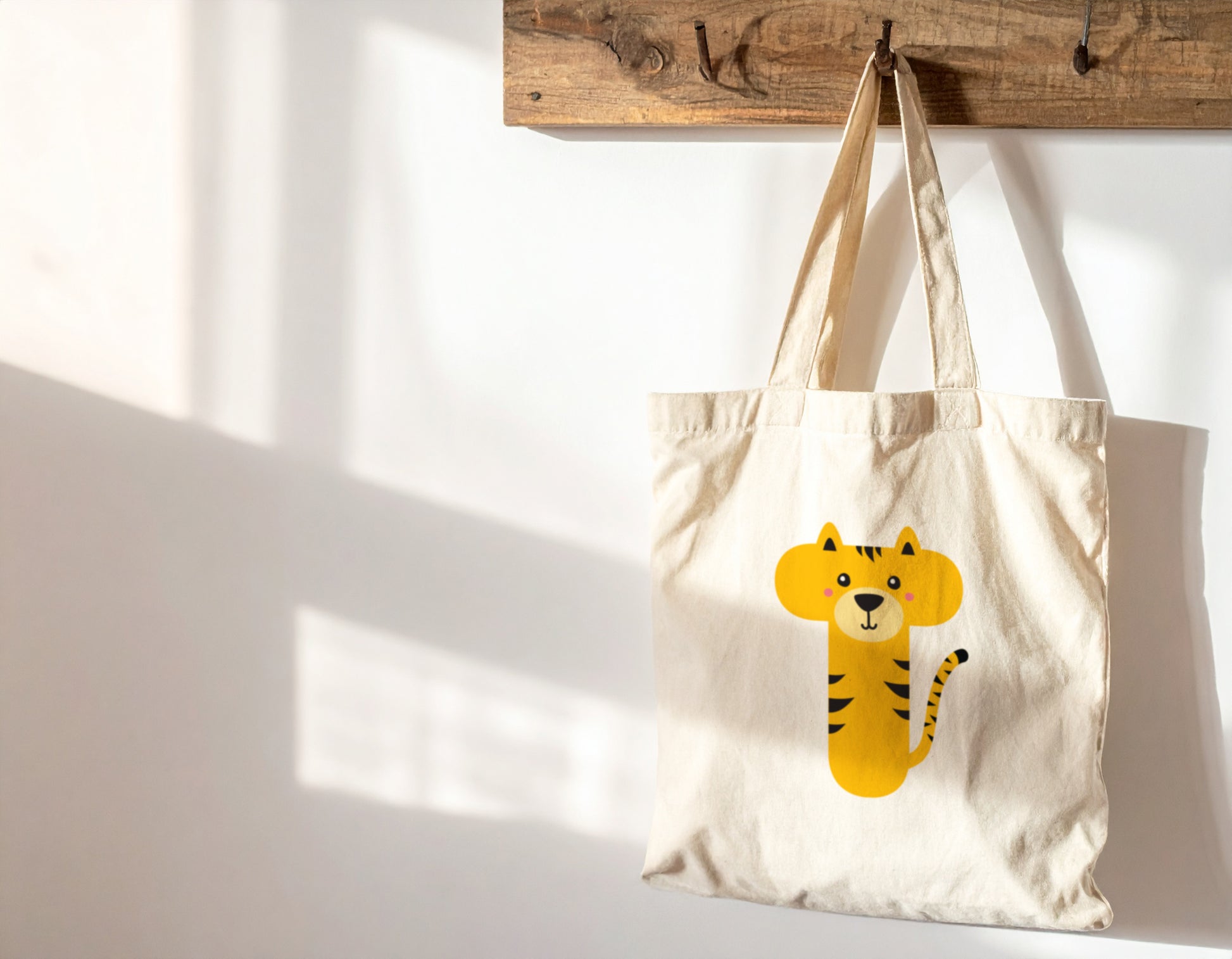 An oyster tote bag with the letter “T” in the shape of a tiger illustration, hanging on a wooden hook against a white wall.
