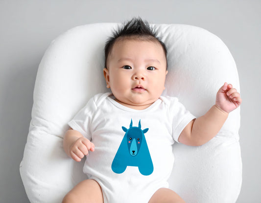 Baby wearing a white organic cotton onesie/bodysuit with the letter A in the shape of an Antelope illustration, sitting on a white cushion on a wooden floor.