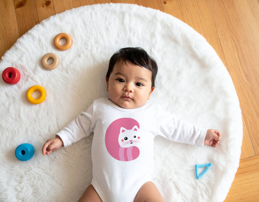 Baby wearing a white organic cotton onesie/bodysuit with the letter C in the shape of a cat illustration, sitting on a white carpet on a wooden floor.