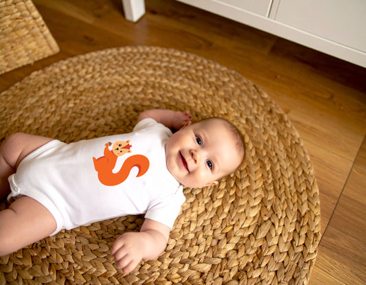 Baby wearing a white organic cotton onesie / bodysuit with the letter S in the shape of a squirrel illustration, lying on a carpet on a wooden floor.