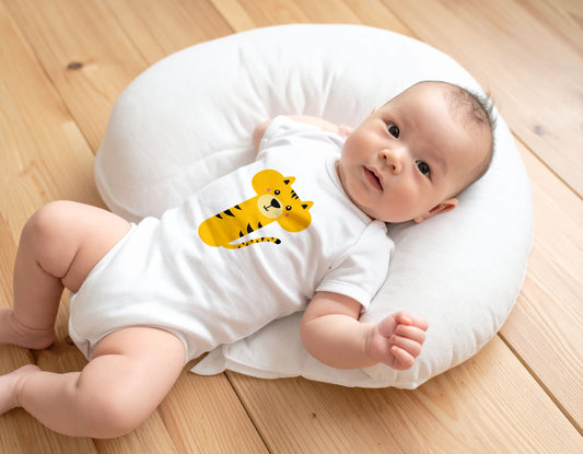 Baby wearing a white organic cotton onesie / bodysuit with the letter T in the shape of a tiger illustration, lying on a boppy pillow on a wooden floor.